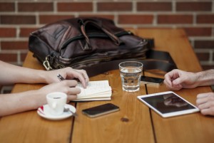 friends-sitting-in-cafe-writing-in-notebook-with-digital-tablet-and-coffee-cup